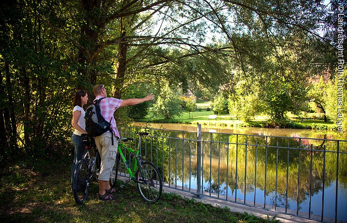 Eisenhammer Am Flussufer der Roth in Eisenhammer genießen zwei Fahrradfahrer den einmaligen Ausblick auf die Roth. Die Roth ist an den Ufern umgeben von grünen Sträuchern und Bäumen.