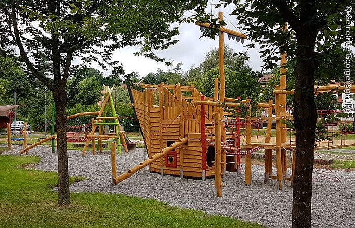 Ein Spielplatz mit einem großem Spielgerät aus Holz. Das Klettergerüst ist in Form eines Schiffes.