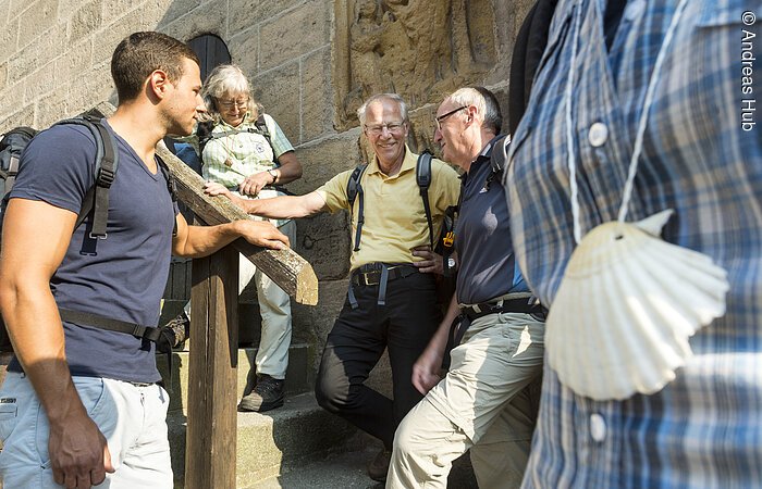 Eine Gruppe Wanderer steht an einer Kirchenwand und unterhält sich.