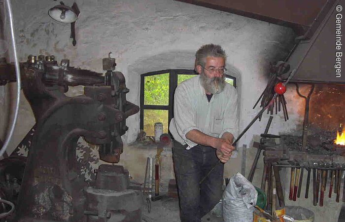 Heiße Ware Ein Mann hält an einer Stange einen rot glühenden Gegenstand in der Hammerschmiede Thalmannsfeld.