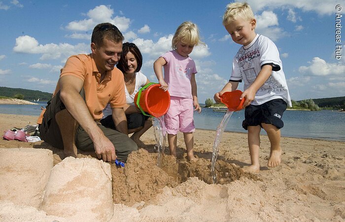 Eine vierköpfige Familie spielt am Strand des Brombachsees in Ramsberg. Die zwei Kinder erfreuen sich am sandeln und genießen die Zeit.