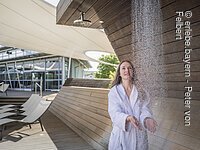 Wasserfall Saunagarten Frau im Bademantel hält ihre Hände unter den Wasserfall