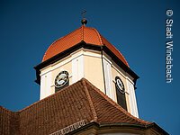 Blick von unten auf eine Kirchturmspitze. Ein Turm mit weiß-gelber Fassade und rotem Haubendach.