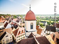 Blick von oben auf den Kirchturm der Stadtkirche Windsbach. Ein Turm mit weißer Fassade und rotem Haubendach.