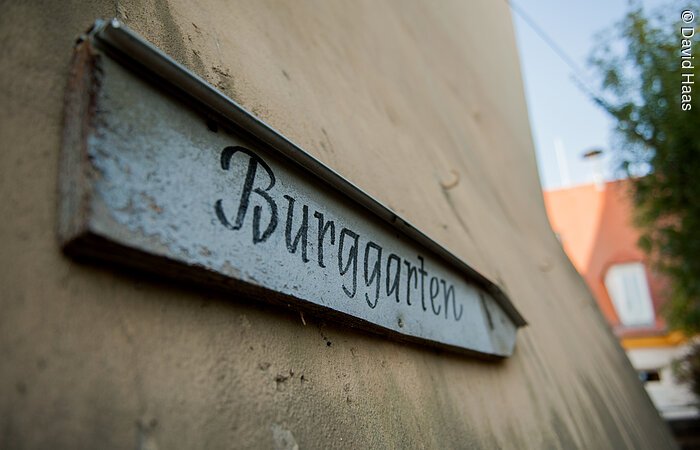 Ein Holzschild an einer Hauswand. Darauf steht in schörkeliger Schrift: Burggarten