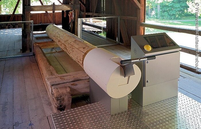 Erlebnispfad - Weg der Wasserkraft Sägespiel im ehemaligen Sägewerk der Mandlesmühle. Ein Baumstamm hängt in einer Sägemaschine.