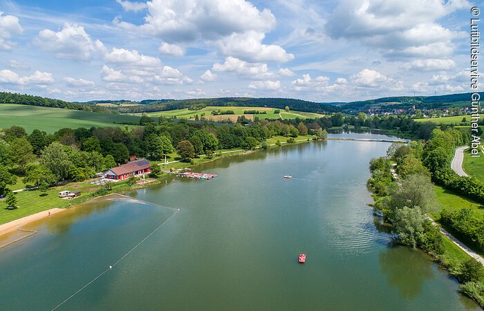 Hahnenkammsee von Süden nach Norden mit Strandanlage links, Seeterasse und Badestrand