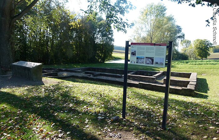 Römische Ruine Eine römische Ruine auf einer grünen Wiese. Davor steht eine Infotafel.