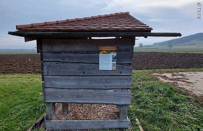 Bewölkter Himmel Kleine offene Holzhütte auf einer Wiese. Dahinter ein braunes Feld. Der Himmel ist bewölkt.