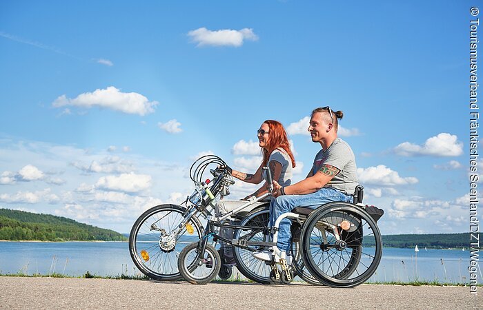 Zwei Handbiker stehen auf dem Damm zwischen dem Kleinen und dem Großen Brombachsee und genießen den Ausblick über die zwei Seen.