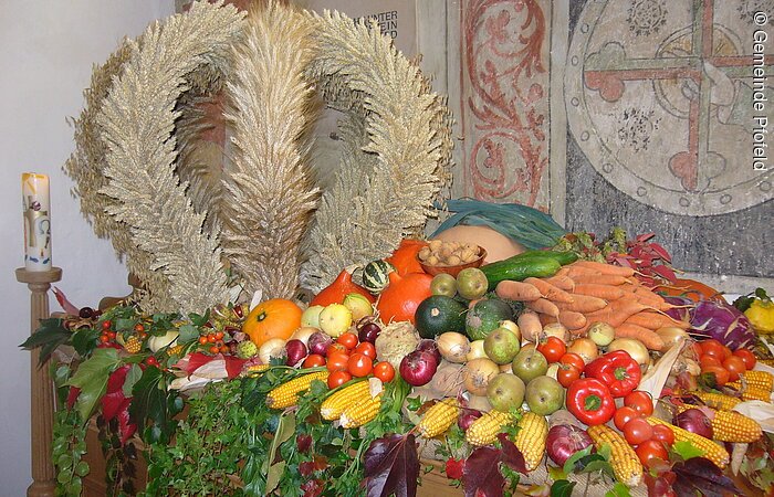 Festlicher Schmuck zum Erntedankfest. Obst und Gemüse platziert auf einem Tisch. Links auf dem Tisch liegt eine Krone geformt aus Getreide.