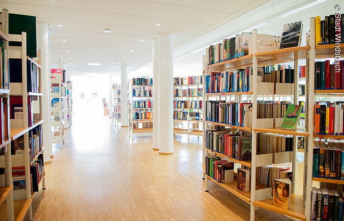 In einem weißen Raum mit Holzparkett stehen Regale mit Büchern.