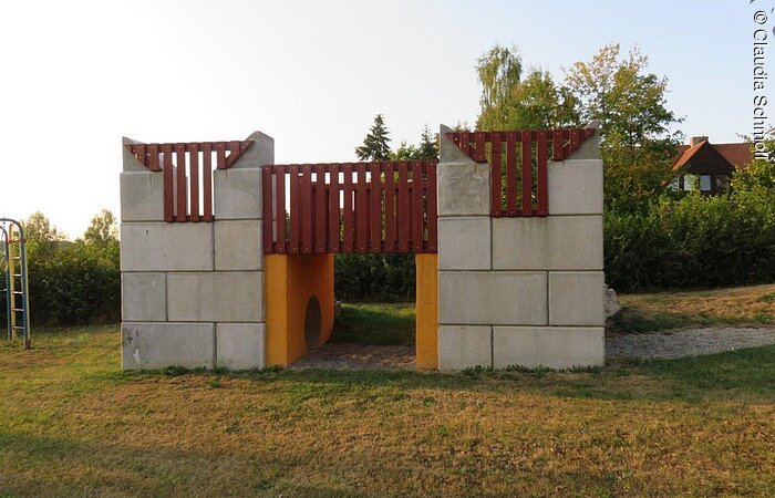 Auf einem Spielplatz steht eine Ausichtsplattform aus Stein. Darunter hindurch führt ein Tunnel durch.